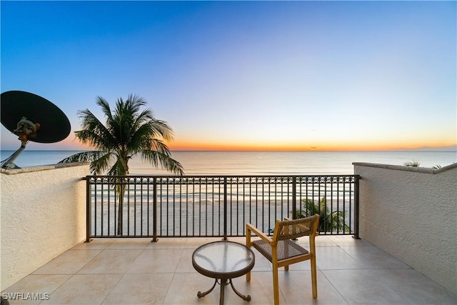 balcony at dusk featuring a water view