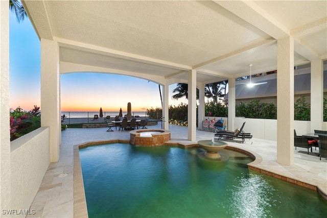 pool at dusk with a patio, a water view, and an in ground hot tub