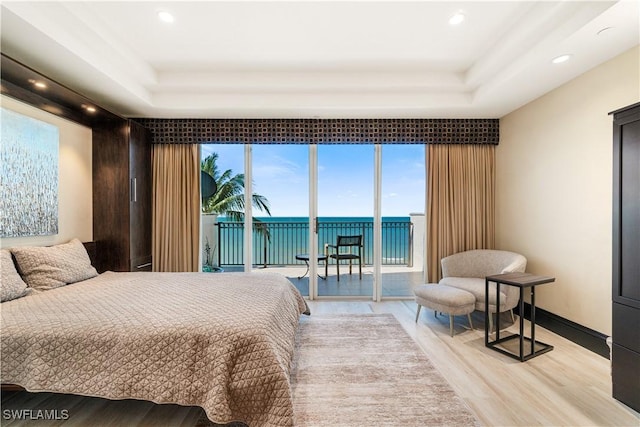 bedroom with a water view, light hardwood / wood-style flooring, access to exterior, and a tray ceiling