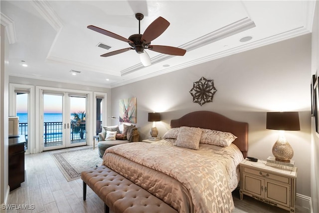 bedroom featuring access to outside, light hardwood / wood-style floors, a tray ceiling, crown molding, and a water view