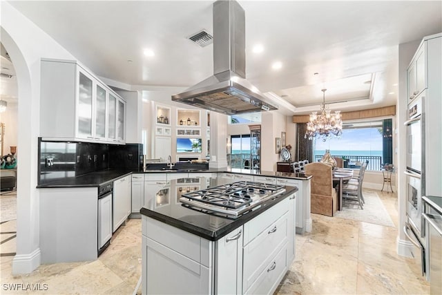 kitchen with hanging light fixtures, stainless steel appliances, white cabinets, island exhaust hood, and a raised ceiling