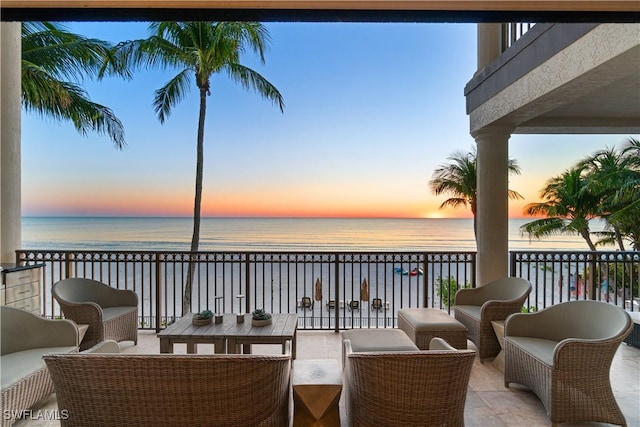 patio terrace at dusk with an outdoor hangout area, a beach view, a balcony, and a water view