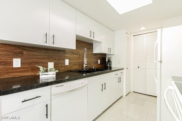 kitchen featuring tasteful backsplash, white cabinets, dark stone countertops, white dishwasher, and a sink