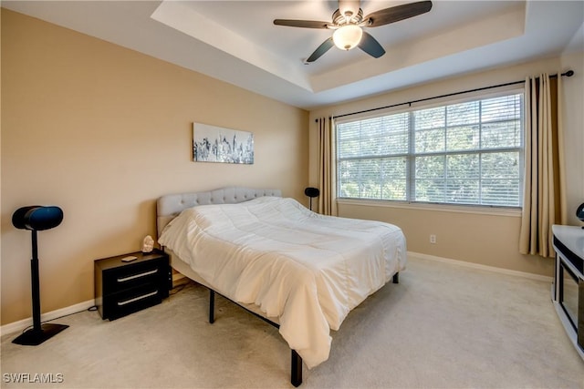 bedroom featuring ceiling fan, light colored carpet, and a tray ceiling