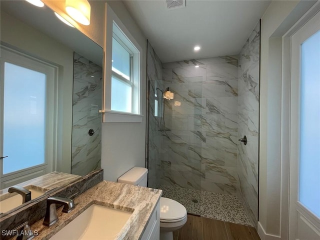 bathroom with vanity, toilet, hardwood / wood-style floors, and a tile shower