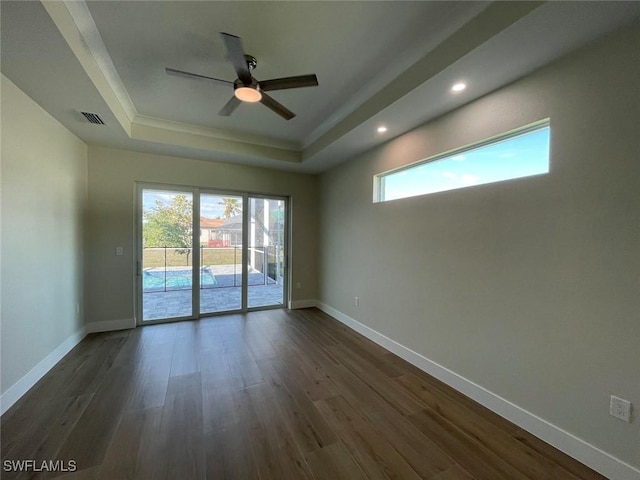 unfurnished room with plenty of natural light, dark wood-type flooring, ceiling fan, and a tray ceiling