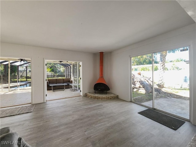 unfurnished living room featuring wood-type flooring, a wood stove, and a healthy amount of sunlight