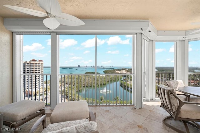 sunroom with ceiling fan and a water view