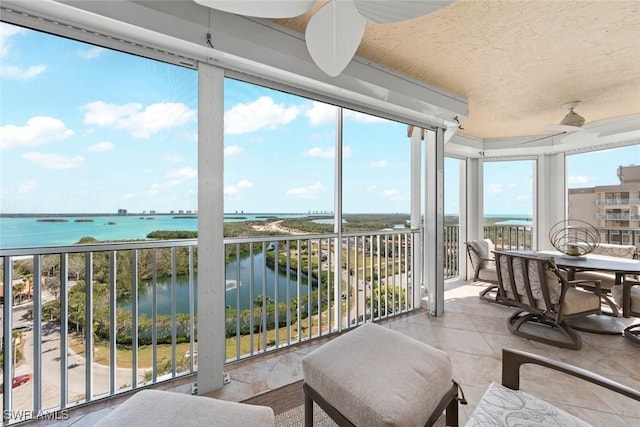 sunroom with ceiling fan and a water view