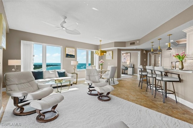 living room with ceiling fan, a textured ceiling, and a water view