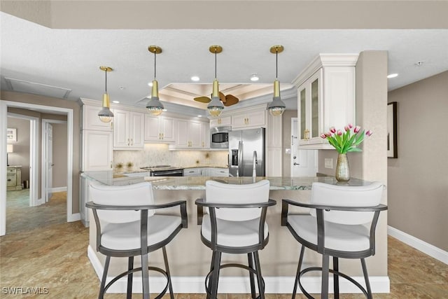 kitchen with stainless steel appliances, light stone counters, tasteful backsplash, white cabinets, and kitchen peninsula