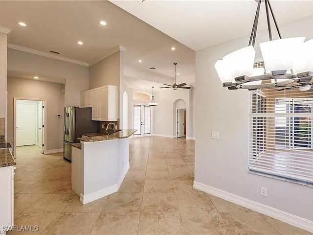 kitchen with hanging light fixtures, ceiling fan with notable chandelier, stainless steel refrigerator, and dark stone counters