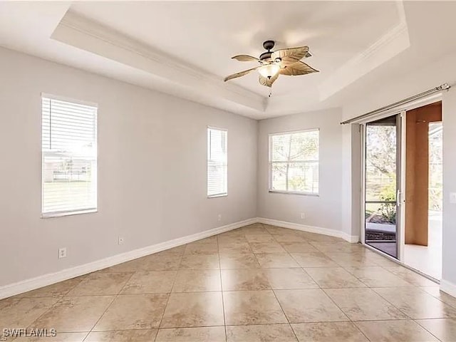 tiled empty room with a raised ceiling, ornamental molding, and ceiling fan