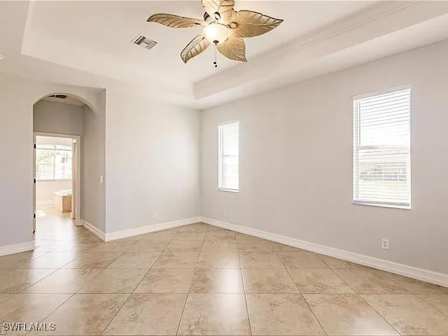 tiled empty room with ceiling fan, plenty of natural light, and a tray ceiling