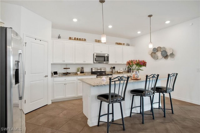 kitchen featuring stainless steel appliances, white cabinetry, hanging light fixtures, and a breakfast bar