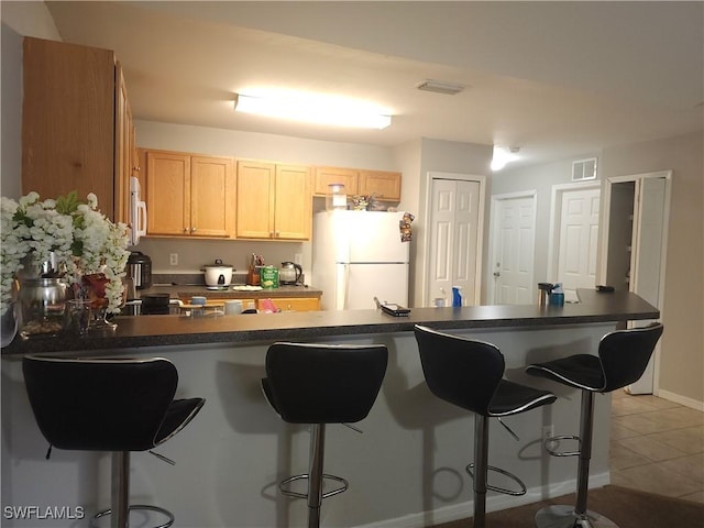 kitchen with white appliances, a breakfast bar, light brown cabinets, and light tile patterned floors