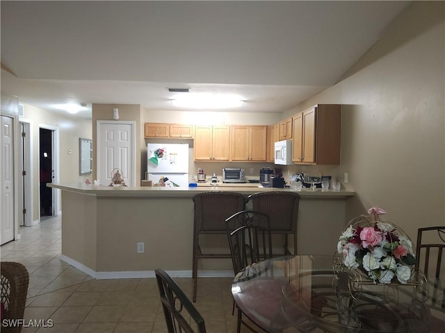 kitchen with light tile patterned floors, light brown cabinetry, white appliances, and kitchen peninsula