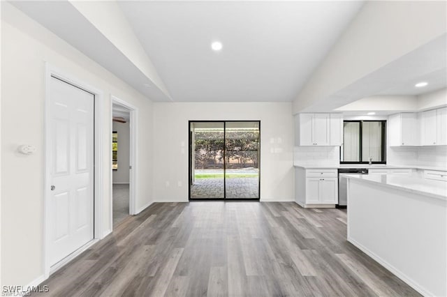 kitchen with lofted ceiling, light wood-type flooring, dishwasher, white cabinets, and backsplash