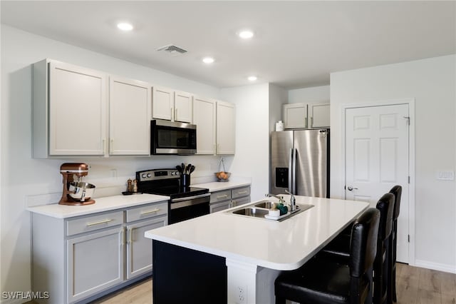 kitchen with appliances with stainless steel finishes, sink, gray cabinetry, a kitchen breakfast bar, and a kitchen island with sink