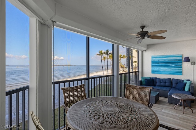 sunroom with a water view, a beach view, and ceiling fan