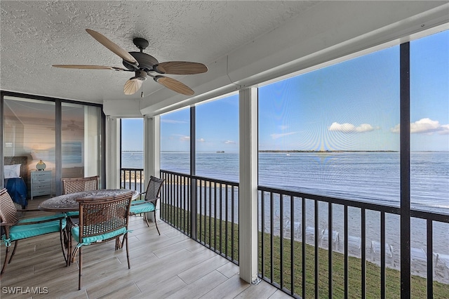 sunroom / solarium with ceiling fan and a water view