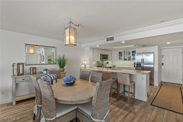 dining area with crown molding, sink, and light hardwood / wood-style flooring