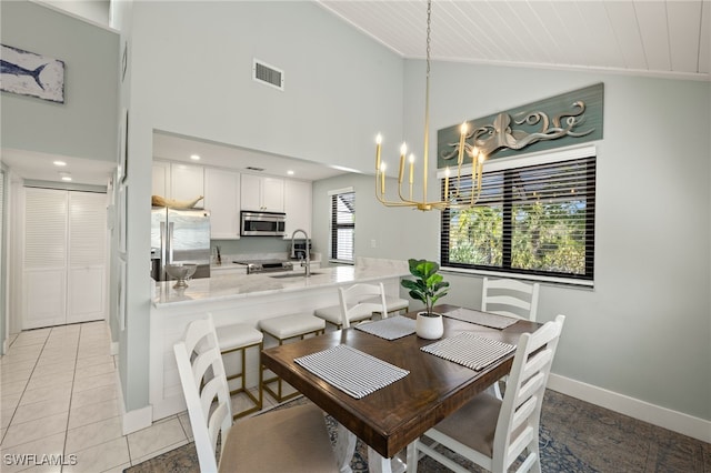 dining room with an inviting chandelier, sink, light tile patterned floors, and high vaulted ceiling