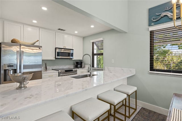 kitchen with sink, light stone counters, white cabinetry, a kitchen breakfast bar, and stainless steel appliances