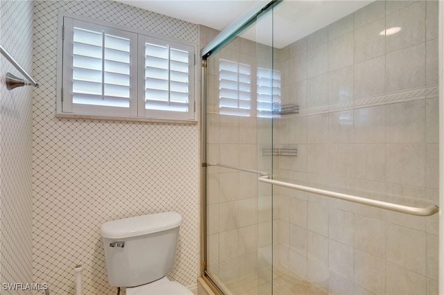 bathroom with a shower with door, tile walls, and toilet