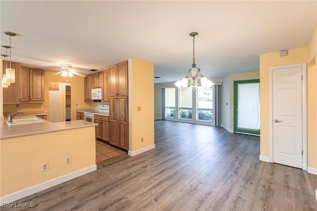 kitchen featuring sink, white appliances, light hardwood / wood-style flooring, decorative light fixtures, and kitchen peninsula