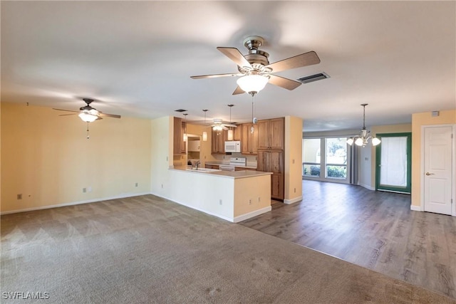 kitchen with sink, white appliances, carpet, ceiling fan with notable chandelier, and kitchen peninsula