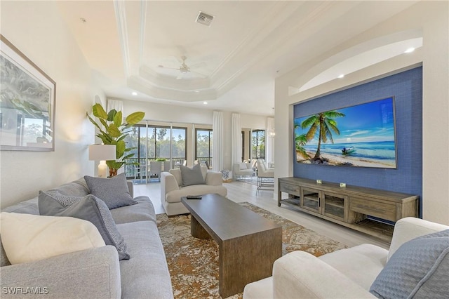 living room featuring ceiling fan, ornamental molding, a raised ceiling, and light hardwood / wood-style floors