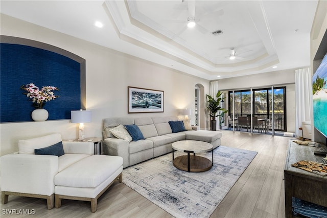 living room with a tray ceiling, wood finished floors, visible vents, and crown molding