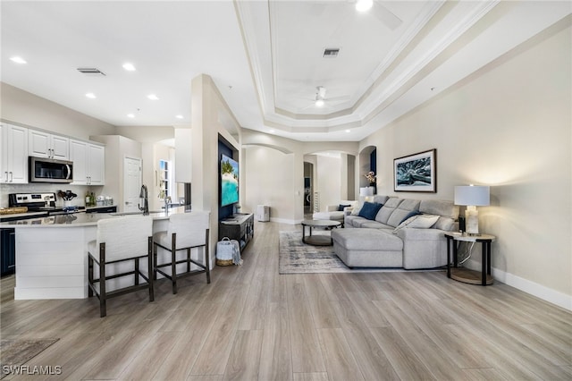 living room with light wood-style floors, baseboards, arched walkways, and crown molding