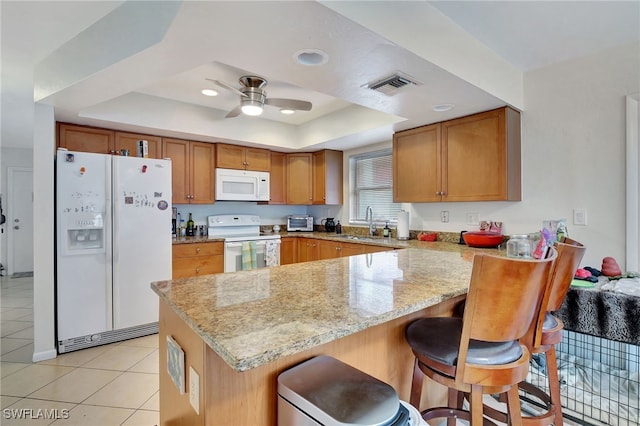 kitchen featuring white appliances, a kitchen bar, a raised ceiling, and kitchen peninsula