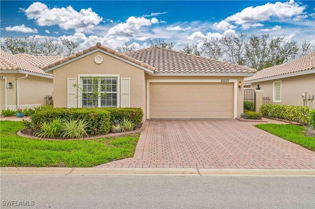 mediterranean / spanish-style house featuring an attached garage, a tile roof, decorative driveway, and stucco siding