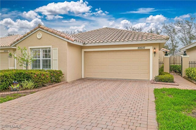 mediterranean / spanish-style home with decorative driveway, stucco siding, a gate, a garage, and a tiled roof