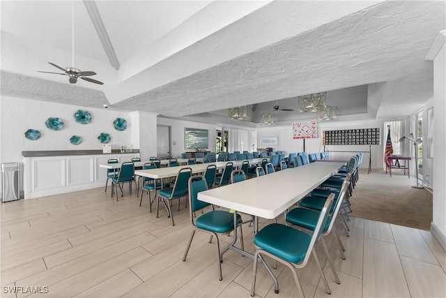 dining space with lofted ceiling, light hardwood / wood-style flooring, ceiling fan, a textured ceiling, and a raised ceiling