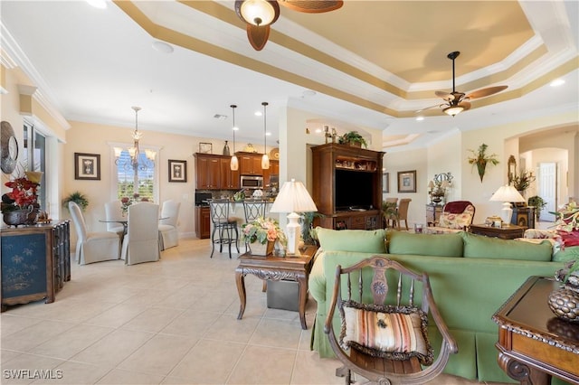 tiled living room featuring ornamental molding, ceiling fan with notable chandelier, and a tray ceiling