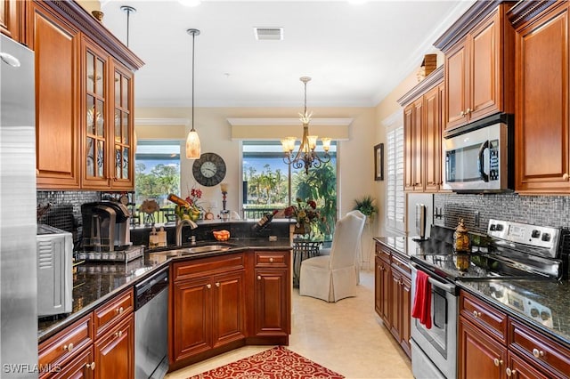 kitchen with decorative light fixtures, sink, dark stone countertops, ornamental molding, and stainless steel appliances