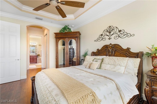 bedroom with crown molding, dark hardwood / wood-style floors, ensuite bath, and a raised ceiling