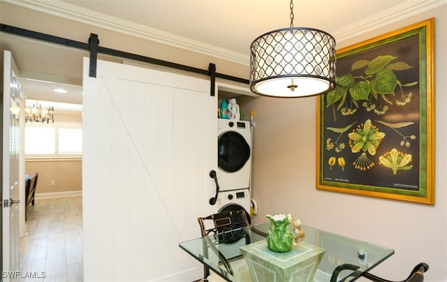 office area featuring wood-type flooring, ornamental molding, a barn door, and stacked washing maching and dryer