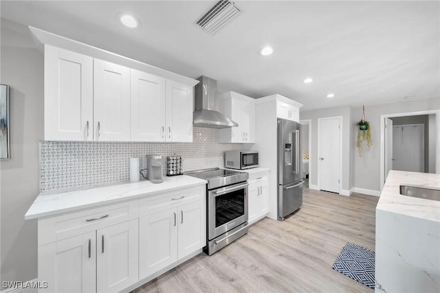 kitchen with white cabinetry, appliances with stainless steel finishes, wall chimney range hood, and light stone counters