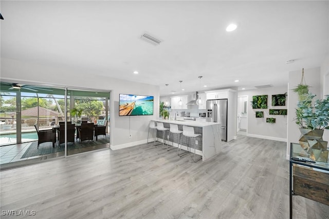 kitchen featuring stainless steel refrigerator with ice dispenser, a breakfast bar, hanging light fixtures, kitchen peninsula, and white cabinets