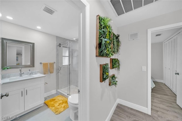 bathroom with hardwood / wood-style flooring, vanity, a shower with shower door, and toilet