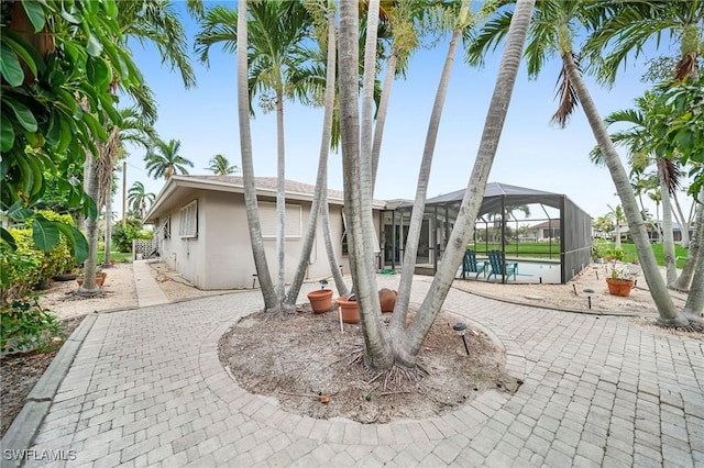 back of property with a pool, a patio area, and glass enclosure