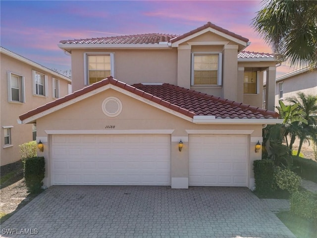 mediterranean / spanish house featuring stucco siding, a tiled roof, and decorative driveway
