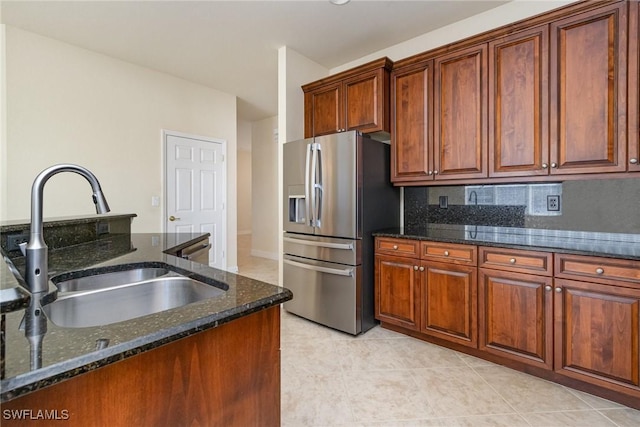kitchen with brown cabinets, dark stone countertops, a sink, light tile patterned flooring, and stainless steel refrigerator with ice dispenser