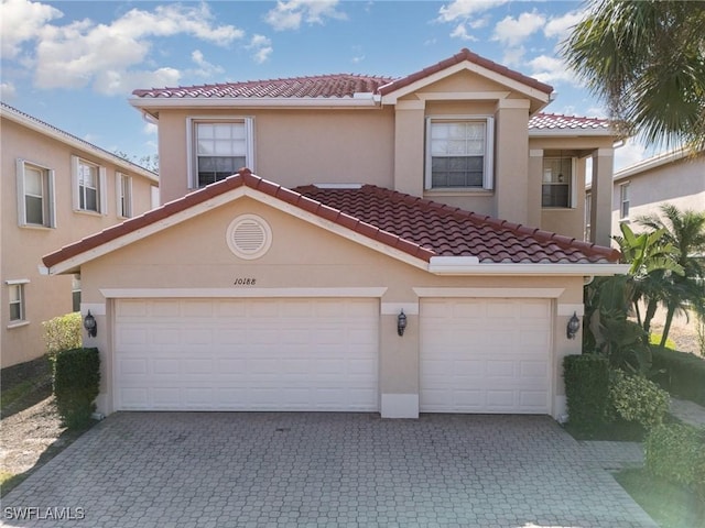 mediterranean / spanish home with stucco siding, an attached garage, a tiled roof, and decorative driveway