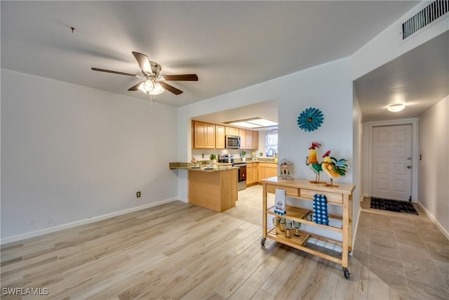 kitchen with appliances with stainless steel finishes, light hardwood / wood-style flooring, light stone countertops, light brown cabinets, and kitchen peninsula